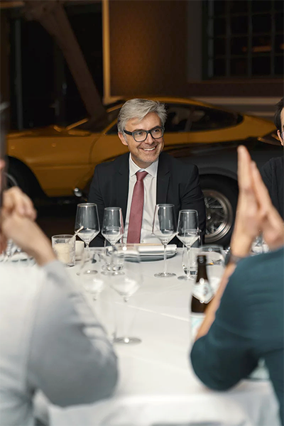 Catering-München. Drei Männer in Anzügen sitzen an einem Tisch mit Gläsern.